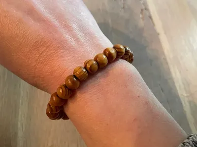 Vorschau: Armband aus Holzperlen mit Maserung wie Baumringe, getragen am Handgelenk über einem Holztisch