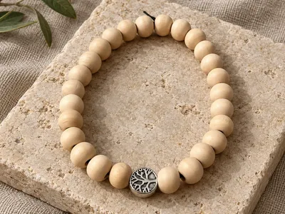 Vorschau: Holzperlen-Armband mit Lebensbaum-Perle auf einem hellen Naturstein, daneben Olivenzweige