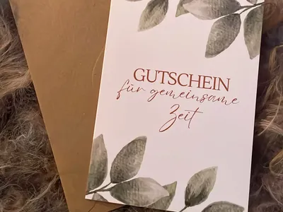 Vorschau: Klappkarte „Gutschein für gemeinsame Zeit“ mit Kraftpapier-Umschlag auf einem hellen Fell