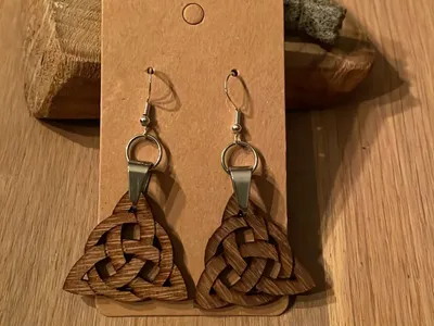 Vorschau: Ohrringe mit geflochtener Triquetra aus Walnussholz an Silberhaken, Schmuckkärtchen auf einem Holztisch