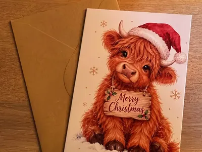 Vorschau: Klappkarte „Highland-Kälbchen mit Mütze“ mit Umschlag aus Kraftpapier auf einem Holztisch