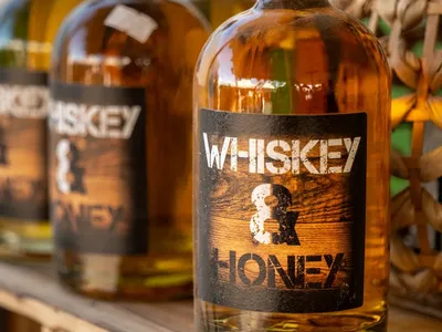 Vorschau: Flasche Whiskey & Honey – Likör, 0,5 l – auf einer alten Holzkiste, dahinter weitere Flaschen