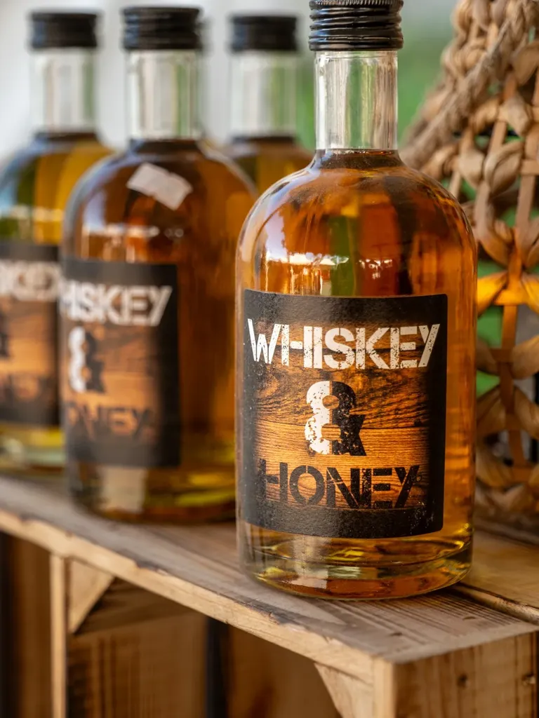 Flasche Whiskey & Honey – Likör, 0,5 l – auf einer alten Holzkiste, dahinter weitere Flaschen